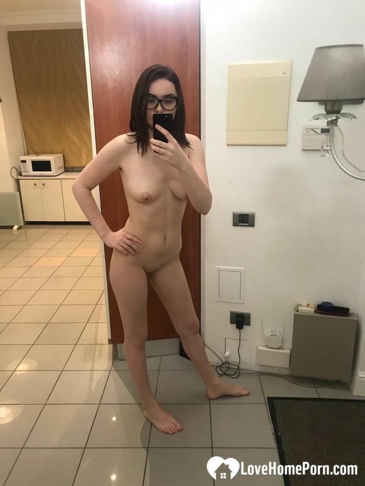 Brünette mit Brille macht Nacktfotos, auf denen sie ihre kleinen Brüste und ihre rasierte Muschi zeigt